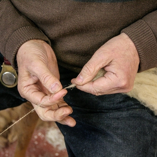 A man wearing a brown sweater is spinning wool into yarn.